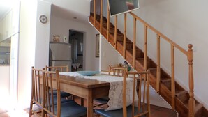 Een eetgedeelte met een houten tafel en stoelen, een trap en een keuken op de achtergrond.