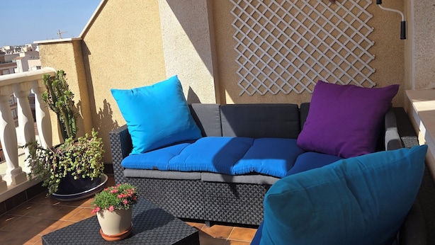 Ein Sitzbereich im Freien mit einer Couch und Sesseln, einem Topf mit einer Pflanze und einer Spalierwand.