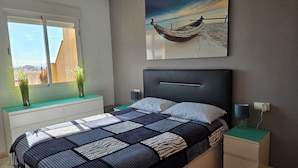 Ein modernes Schlafzimmer mit einem großen Bett, Nachttischen, einem Fenster mit Ausblick und einem Gemälde eines Bootes an der Wand.