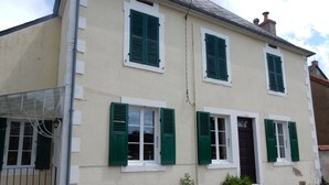 A two-story building with green shutters, a white facade, and a small garden area with potted plants. - Beautiful, quiet, Burgundy village location close to local amenities. (Panneçot)