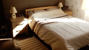 A bedroom with a bed, a nightstand, a lamp, a framed picture on the wall, and a patterned curtain. - Beautiful, quiet, Burgundy village location close to local amenities. (Panneçot)