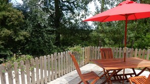 A patio with a wooden table and chairs, a red umbrella, and a white picket fence. - Beautiful, quiet, Burgundy village location close to local amenities. (Panneçot)