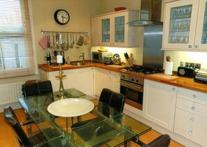 Una cucina con un tavolo da pranzo in vetro, mobili bianchi, un fornello e diversi utensili da cucina.