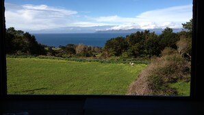 A view from a window overlooking a grassy field with trees and a distant body of water.