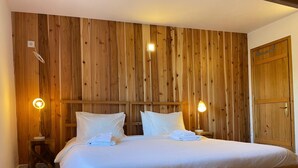 A wooden-paneled bedroom with a bed, two bedside lamps, and a wooden wardrobe.
