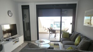 A living room with a flat-screen TV, a sofa, a coffee table, and a dining area with chairs and a table. - Holiday Houses - Los Altos 92 (Torrevieja)