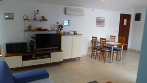 A living room with a TV, sofa, dining table, chairs, and a kitchen area with cabinets and a refrigerator. - APARTMENT GROZIĆ **** PORAT - KRK  (MALINSKA)