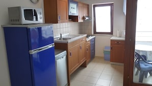 A compact kitchen with a blue refrigerator, a microwave, a sink, and wooden cabinets. - APARTMENT GROZIĆ **** PORAT - KRK  (MALINSKA)