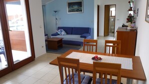 A dining area with a wooden table and chairs, a blue sofa, and a painting on the wall. - APARTMENT GROZIĆ **** PORAT - KRK  (MALINSKA)