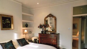 A bedroom with a large bed, a dresser with a mirror, a nightstand, a lamp, and a framed picture on the wall.