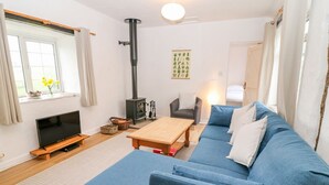 A cozy living room with a blue sofa, a wooden coffee table, a TV, and a fireplace. - Granary - 17th century converted cottage (Looe)