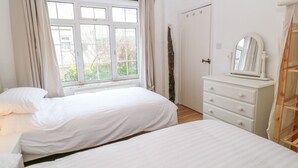 A bedroom with two beds, a dresser, a mirror, and a window with curtains. - Granary - 17th century converted cottage (Looe)