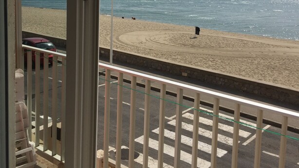 A beach view from a balcony with a railing, a street with cars, and a clear sky. - For rent T2- Leucate plage - 1er D- Front de mer (Leucate)