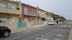 A street with buildings, a blue gate, and a white car. - For rent T2- Leucate plage - 1er D- Front de mer (Leucate)