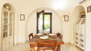 A dining area with a wooden table set for four, flanked by chairs. An arched doorway leads to an outdoor area.