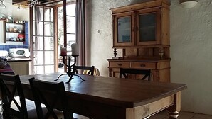 Un comedor con una mesa y sillas de madera, un armario y un ventanal con cortinas.