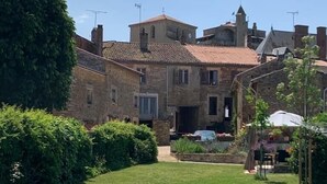 Una piscina con superficie de agua cristalina azul, rodeada de un césped cuidado y un edificio de piedra con múltiples ventanas y tejado de tejas.