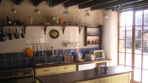 Una cocina con estufa, horno, microondas y taburetes de bar. Hay estantes con vajilla y un reloj en la pared.
