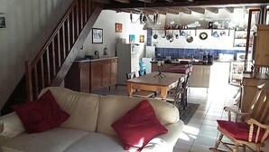 Una sala de estar con sofá y sillones, una mesa de comedor, una cocina al fondo y una escalera.