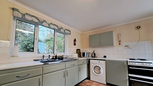 A compact kitchen with a washing machine, a stove, and a microwave. - Little Croft - Spacious cottage in Woodland setting close to fantastic beaches (Truro)