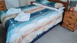 A neatly made bed with a patterned bedspread, two pillows, and folded towels. There is a wooden nightstand with a lamp beside the bed. - Little Croft - Spacious cottage in Woodland setting close to fantastic beaches (Truro)