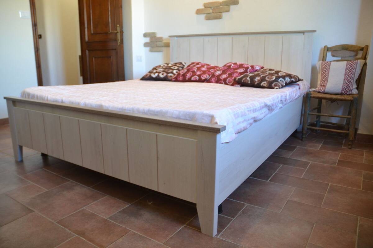 Een slaapkamer met een houten bed, een stoel en een betegelde vloer.