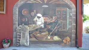 Une fresque représentant une scène de boulangerie, avec une arche en pierre, un chat et divers ustensiles de pâtisserie.