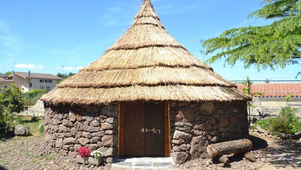 Une cabane en pierre avec un toit de chaume, une porte en bois et un petit seuil menant à l’entrée.