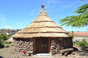 Une cabane en pierre avec un toit de chaume, une porte en bois et un petit seuil menant à l’entrée.