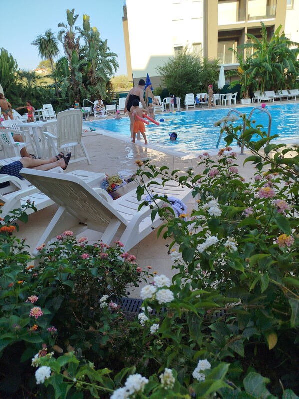 A poolside area with lounge chairs, a swimming pool, and surrounding greenery.