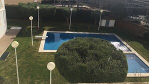 Une piscine entourée de pelouse bien entretenue, une grande structure couverte et un immeuble imposant en arrière-plan.