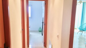 Un couloir au sol carrelé qui mène à une pièce contenant un lit et une fenêtre.