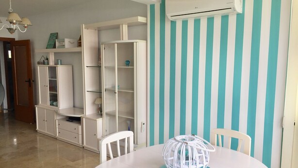 A dining area with a white table, chairs, and a decorative globe centerpiece. There is a white cabinet with glass doors and a teal-striped wall in the background.