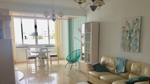 Un salon avec un canapé beige, un fauteuil turquoise, une vitrine et un coin repas comprenant une table et des chaises.