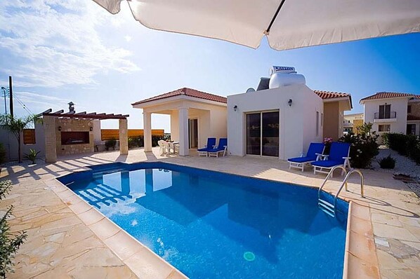 Ein Swimmingpool mit Liegestühlen und Sonnenschirmen, umgeben von Gebäuden im mediterranen Stil.