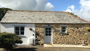 A stone cottage with a white facade, a tiled roof, and a small porch area.