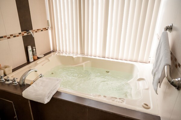 Une salle de bain avec une baignoire, un lavabo et une fenêtre avec des stores.