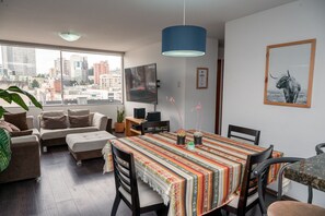 A modern living room with a dining area, large windows, and a city view.
