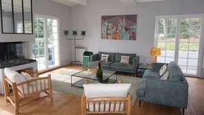 A spacious living room with a fireplace, a green sofa set, wooden chairs, and a glass coffee table. - Villa Biarritz / 5 mn plages / Heated pool (Biarritz)