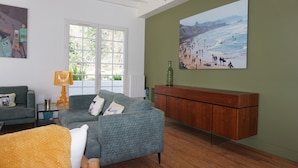 A living room with a grey sofa, a wooden cabinet, and a painting of a beach scene. - Villa Biarritz / 5 mn plages / Heated pool (Biarritz)