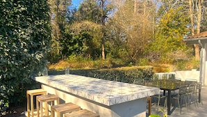 An outdoor kitchen area with a marble countertop, wooden stools, and a dining table with chairs. - Villa Biarritz / 5 mn plages / Heated pool (Biarritz)