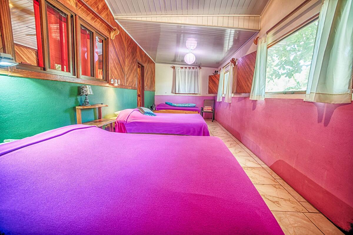 A room with two beds, wooden walls, a window with curtains, and a ceiling light.