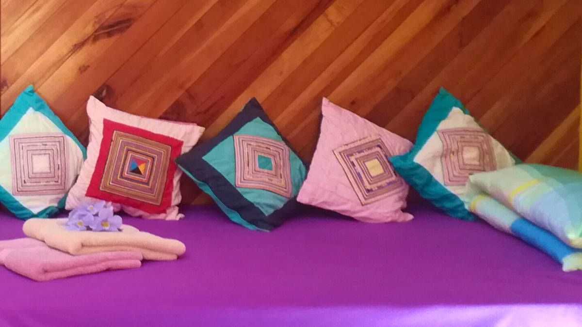 Cama com colcha roxa e cinco almofadas com estampas geométricas.