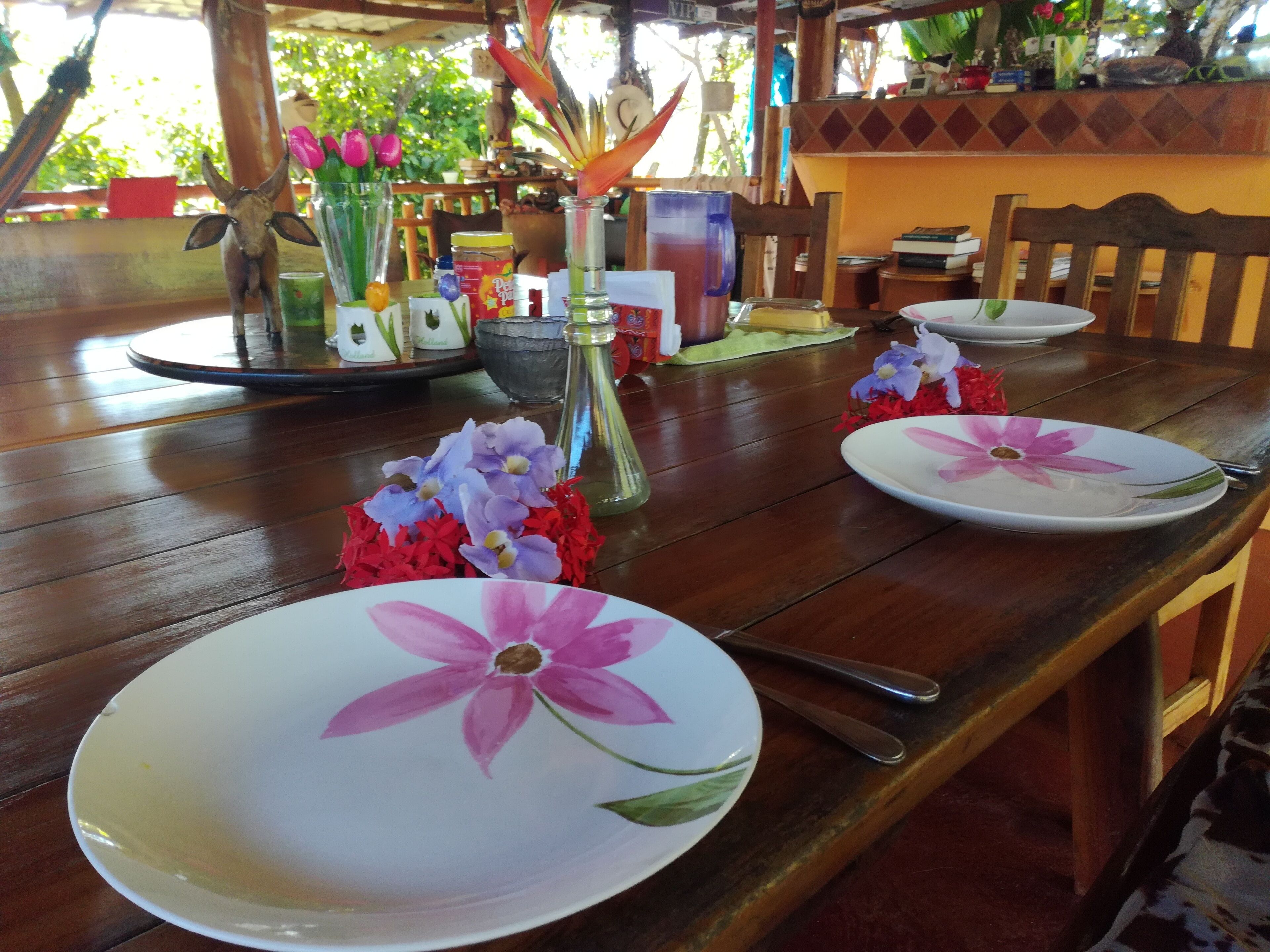 A wooden dining table with floral plates, a glass vase with flowers, and a decorative cow figurine.