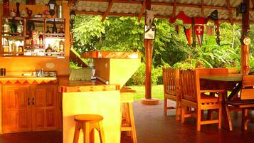 A rustic outdoor bar area with wooden furniture, a sink, and various bottles.