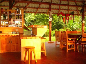 A rustic outdoor bar area with wooden furniture, a sink, and various bottles.