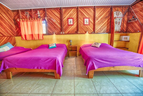 A room with two wooden beds, a small table, and a wall with wooden paneling and framed pictures. - Fidelito Ranch & Lodge (Paquera)