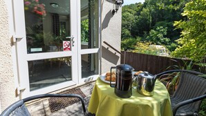 A patio with a table set for breakfast, a coffee pot, and a croissant on a yellow tablecloth. - Two bed Appt. 10 minutes walk to Lynton . Riverside location. EV charge point (Lynton)