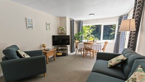 A living room with two sofas, a TV, a small table with a lamp, and a window with curtains. - Two bed Appt. 10 minutes walk to Lynton . Riverside location. EV charge point (Lynton)