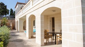 A covered outdoor patio with stone arches, a pool, and wooden furniture.